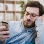 Portrait,Of,Worried,Man,On,The,Sofa,Holding,Cellphone,At