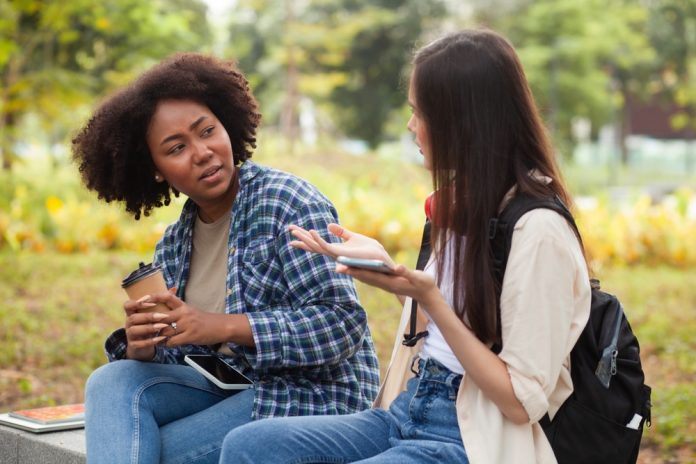 Two,Young,Women,Sitting,On,A,Bench,In,A,Park,
