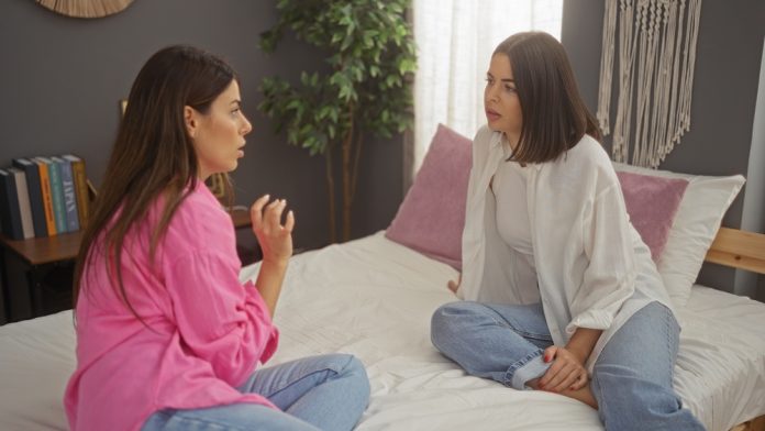 Two,Women,Sitting,On,A,Bed,Having,A,Serious,Conversation